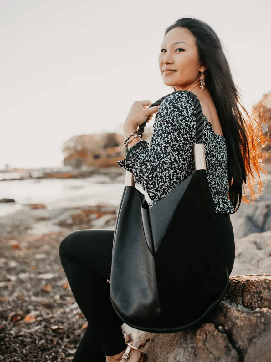 woman sitting on a rock at the beach with a black leather bag