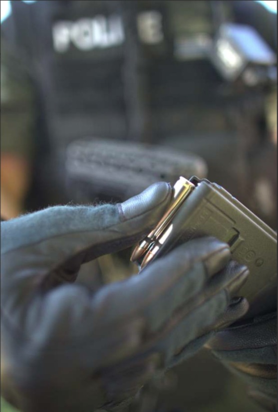 Person in gloves holding a weapon magazine, police gear visible in background.