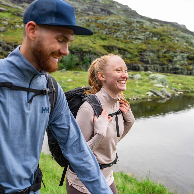 Man & Woman trekking beside river wearing Helly Hansen tech t-shirts.