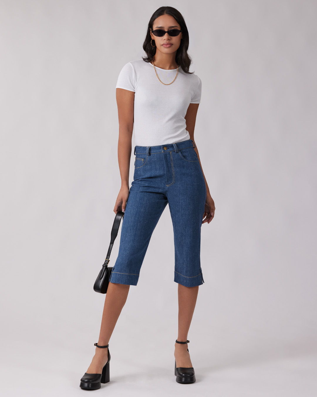 Model wearing a white t-shirt and blue cropped jeans, accessorized with sunglasses.