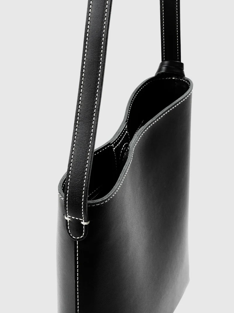 Black leather shoulder bag with white stitching and a minimalist design.