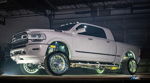 Side profile of lifted white Ram Limited truck with gold suspension, chrome wheels, and wheel well underglow in dark garage
