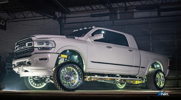 Side profile of lifted white Ram Limited truck with gold suspension, chrome wheels, and wheel well underglow in dark garage