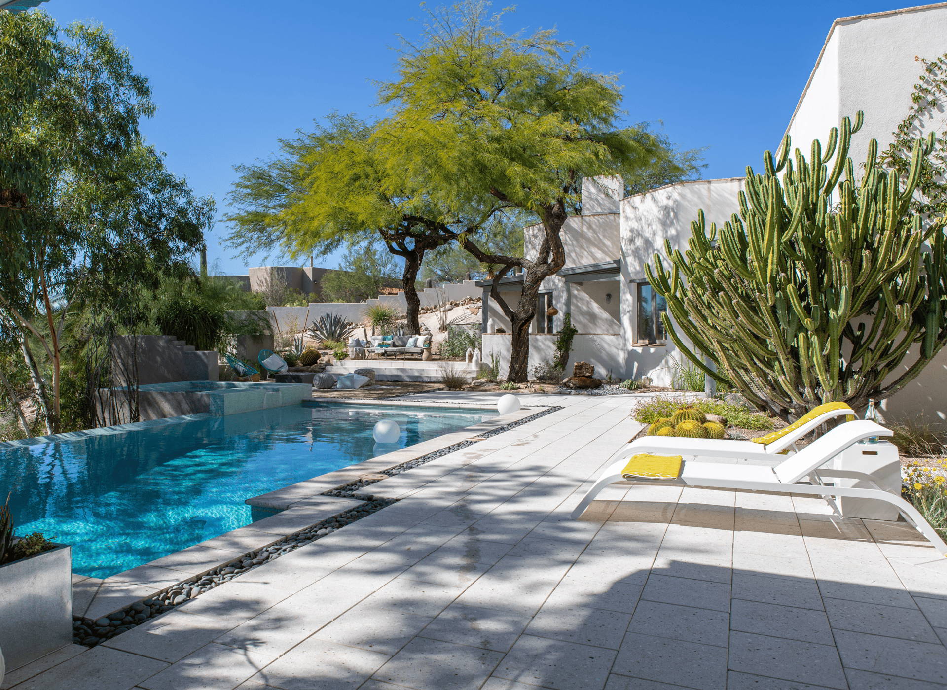 A modern desert patio with white chaise loungers overlooking a pool. 
