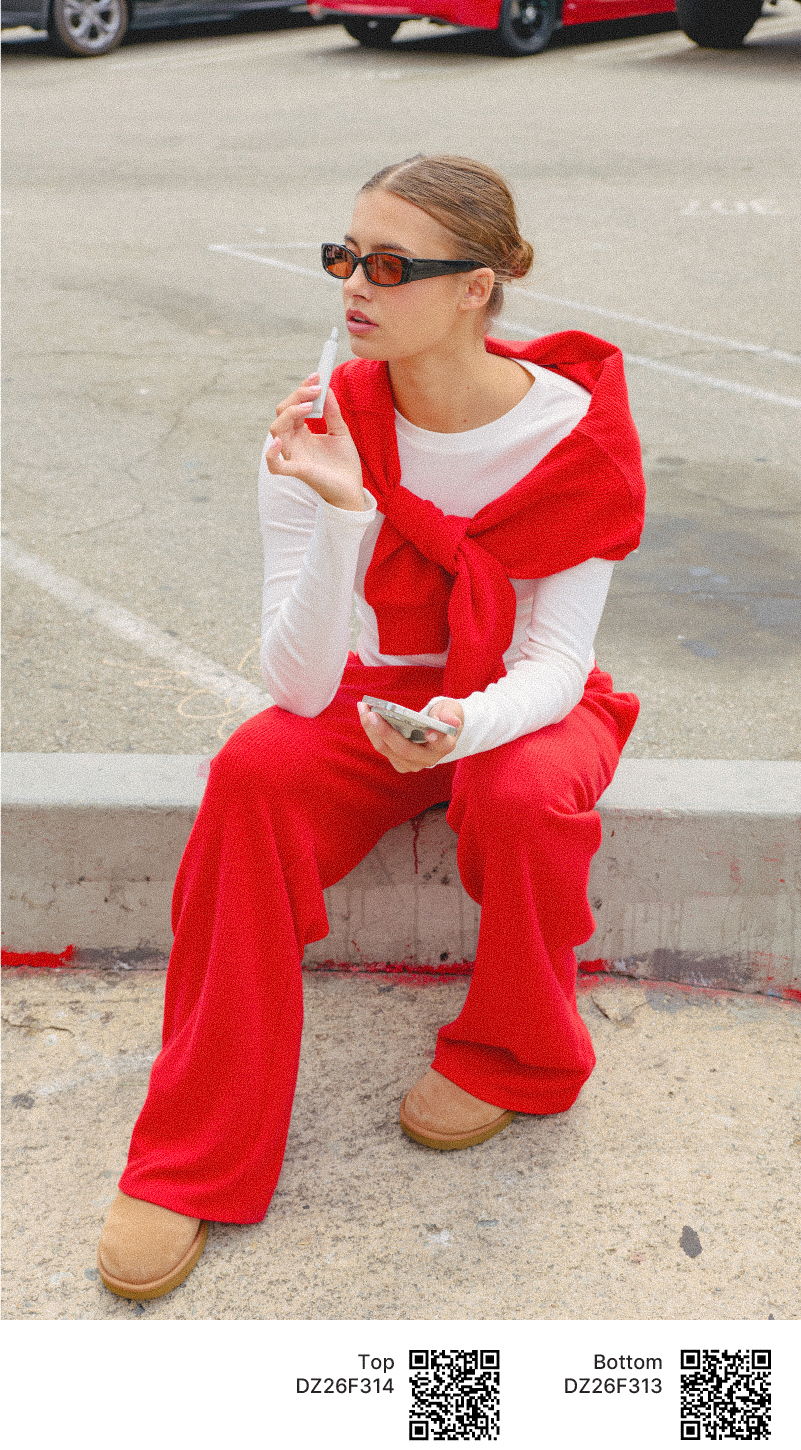 Person in red outfit sitting casually, holding a phone, wearing sunglasses.