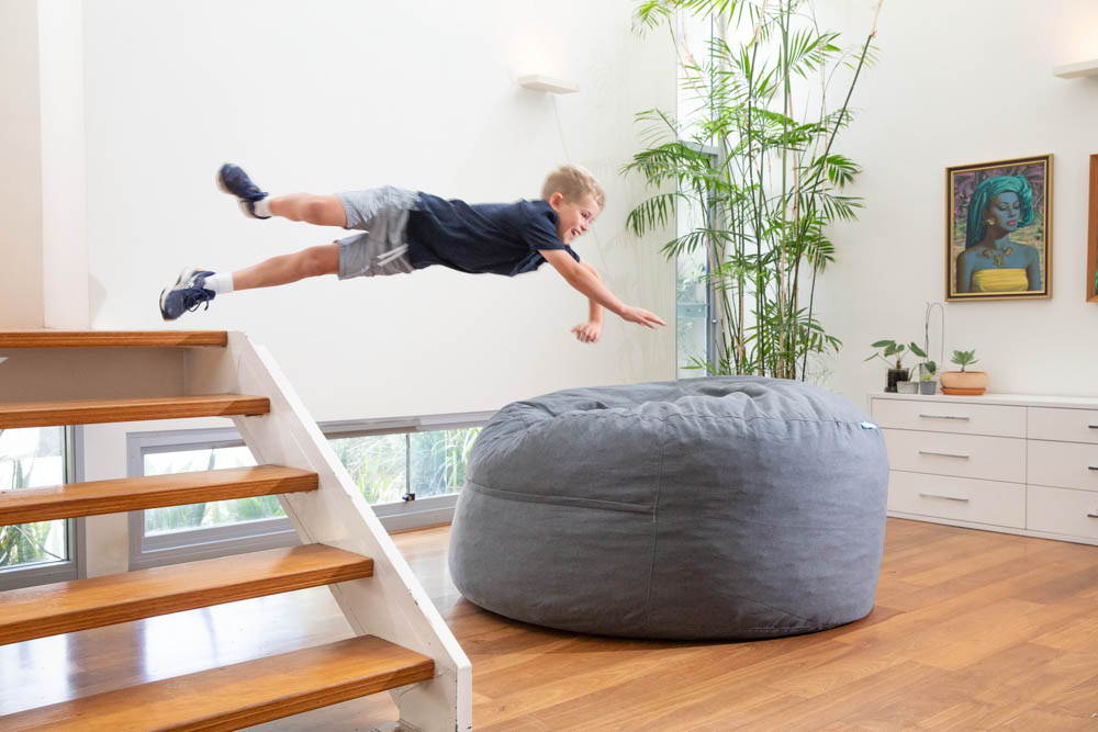 Child jumping into big grey foam filled bean bag