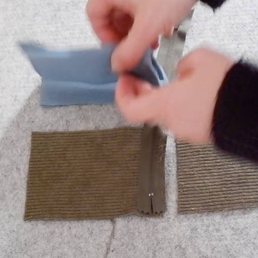 hands folding the fabric on the zipper to sew them together correctly