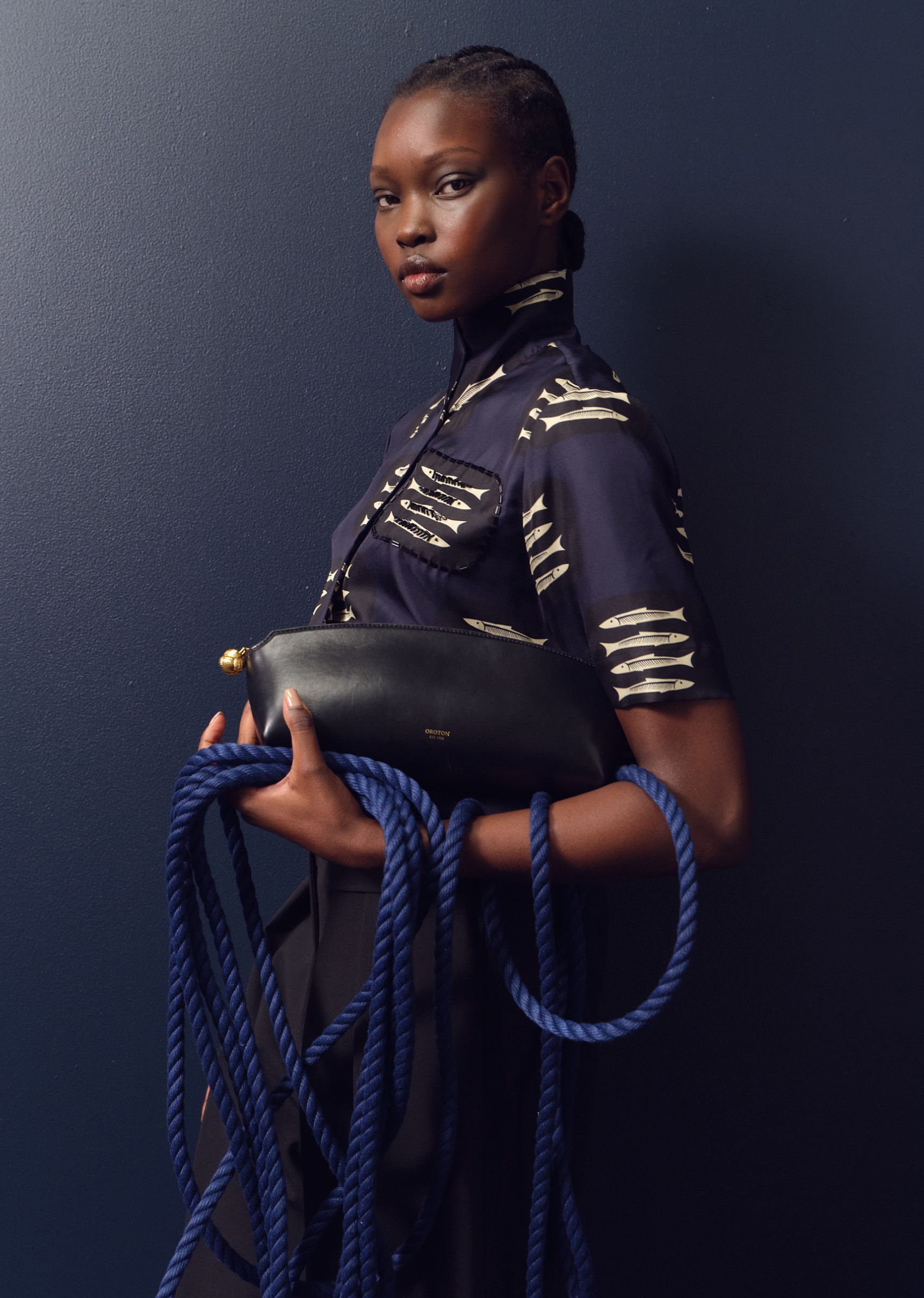 Model holding a black bag and blue ropes against a dark background.