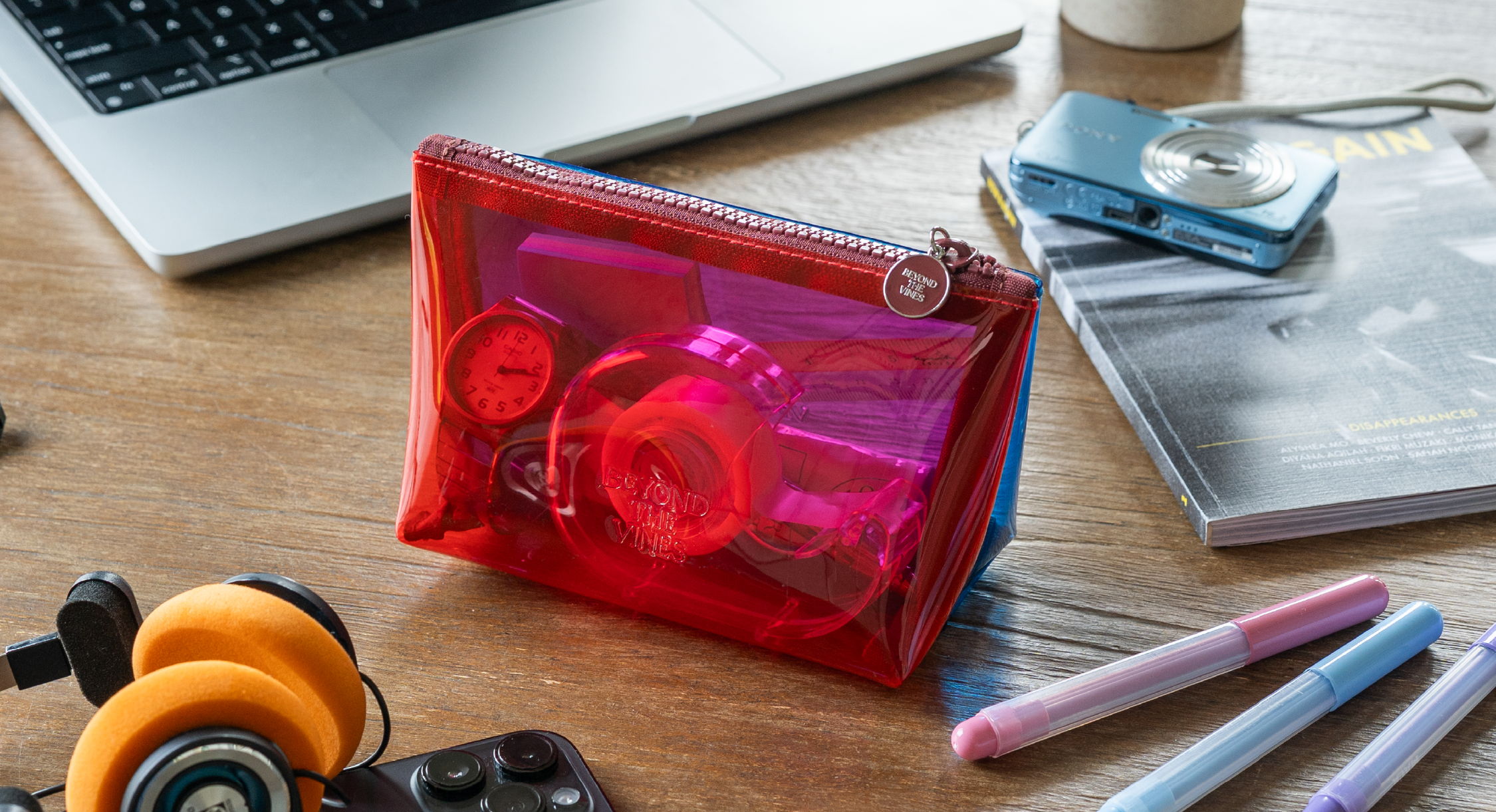 Colorful transparent pouch on a wooden desk with headphones and stationery.
