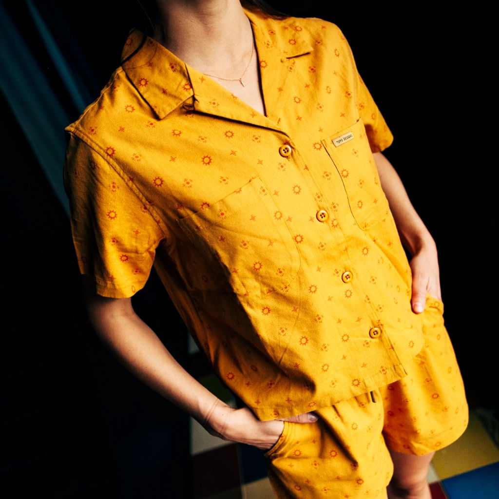 Person wearing a yellow patterned shirt and shorts against a dark background.