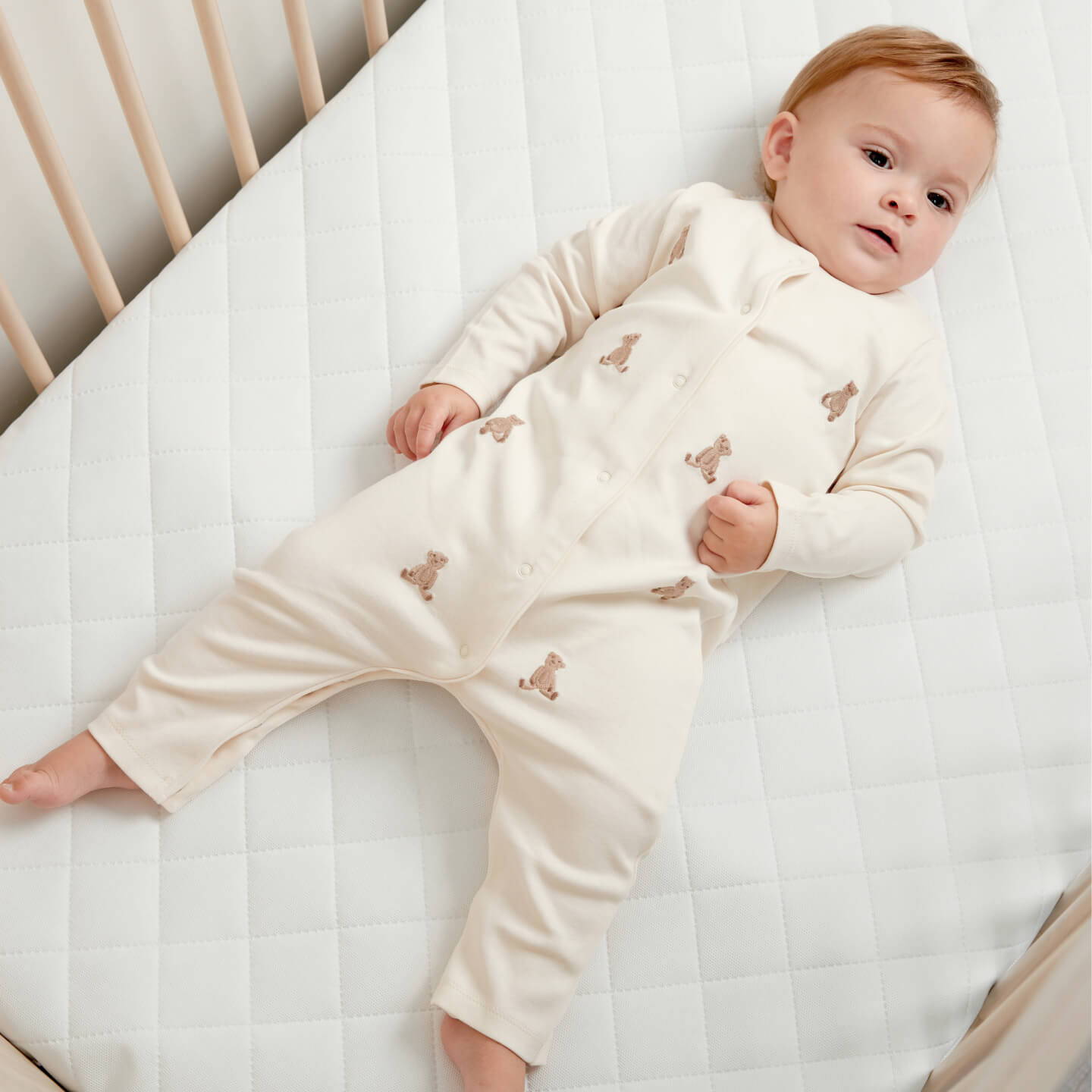 Baby laid on Mamas & Papas mattress in teddy bear all in one