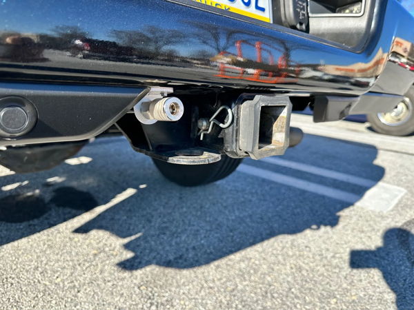 Close-up of rear bumper quick-connect air fitting mounted next to trailer hitch on black truck