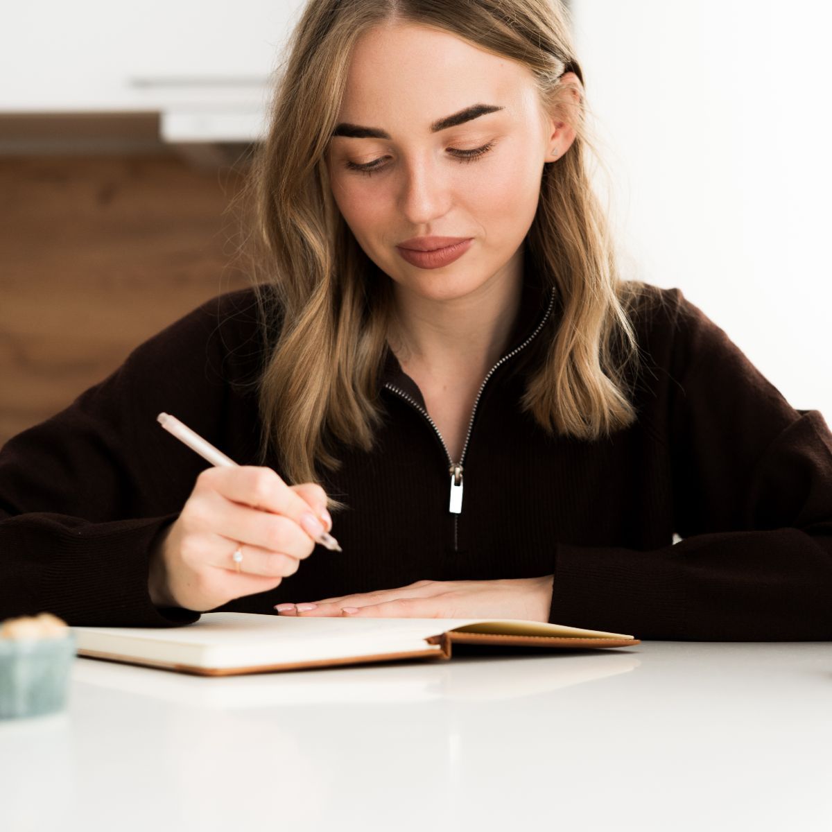 A young woman writing in a journal at a table.