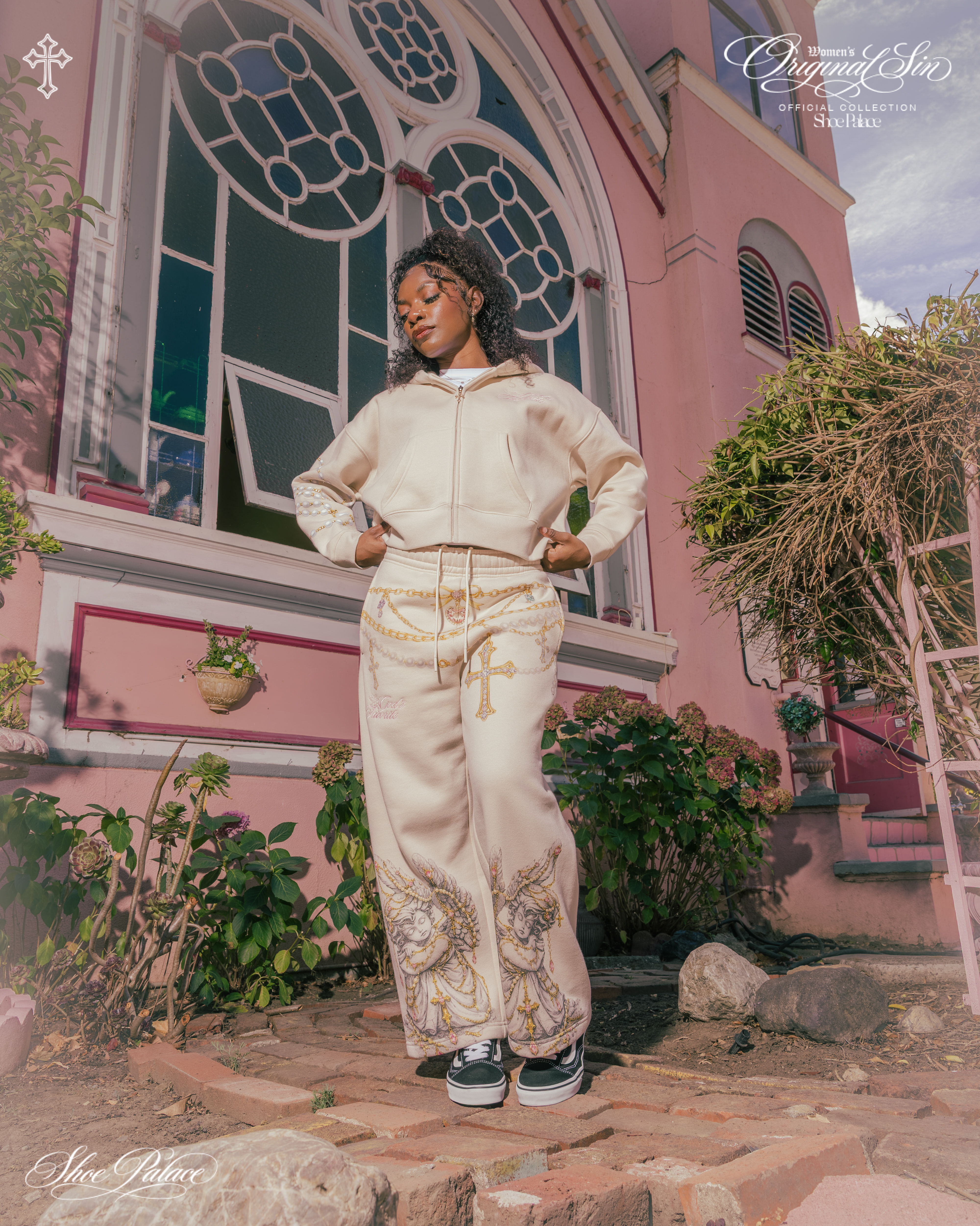Person in stylish outfit posing near a pink building with decorative windows.