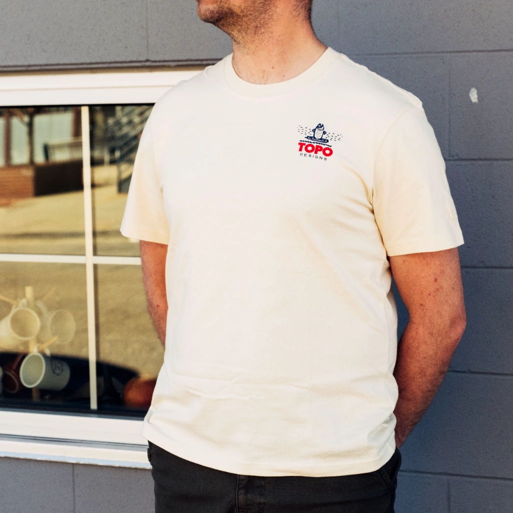 A person wearing a light-colored shirt stands beside a window.