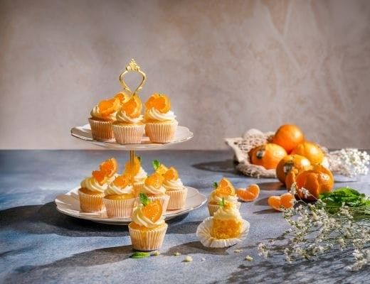 A tiered display of cupcakes topped with orange slices and mint leaves.