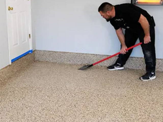 Scraping the dried epoxy floor lightly in a cross-hatch pattern, removing loose flakes for a smooth finish.