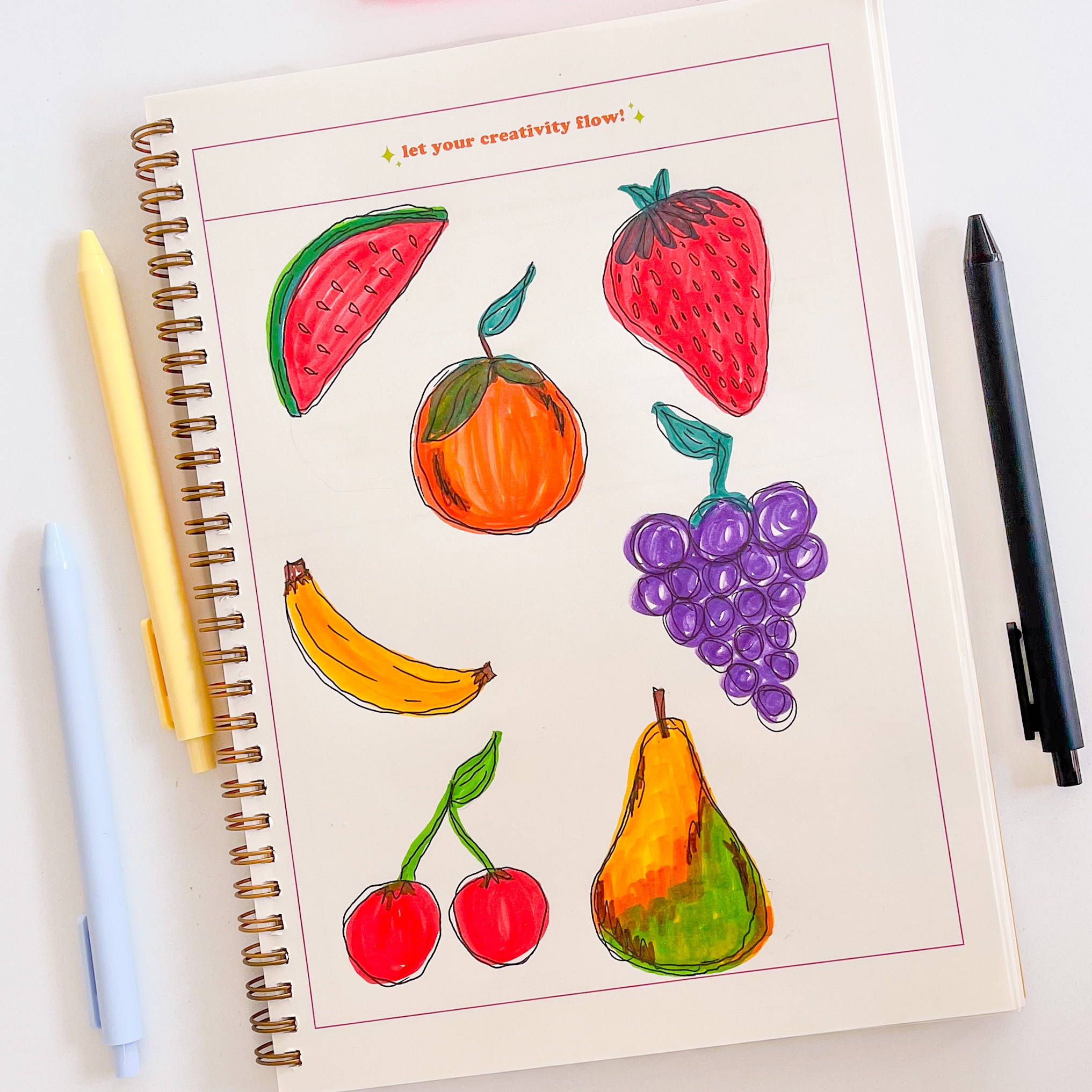 This shows a page out of the Creative Flow Journal. This is the second page of the daily spread and has a large open space with a border around it so you can let your creativity flow! As an example, there is a drawing of different fruit like a strawberry, pear, banana, grapes, cherry, and orange. 