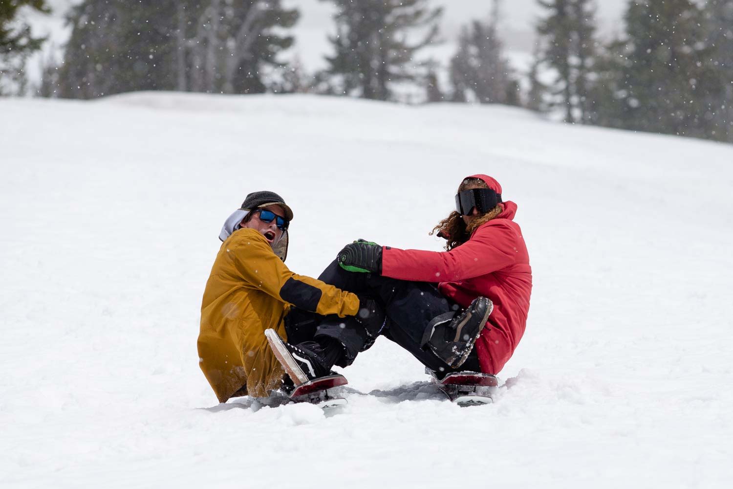 Two people sitting in snow, preparing to snowboard.
