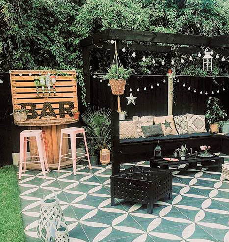 A black pergola with festoon lights hung draped around the edges with a summer bar by the side.