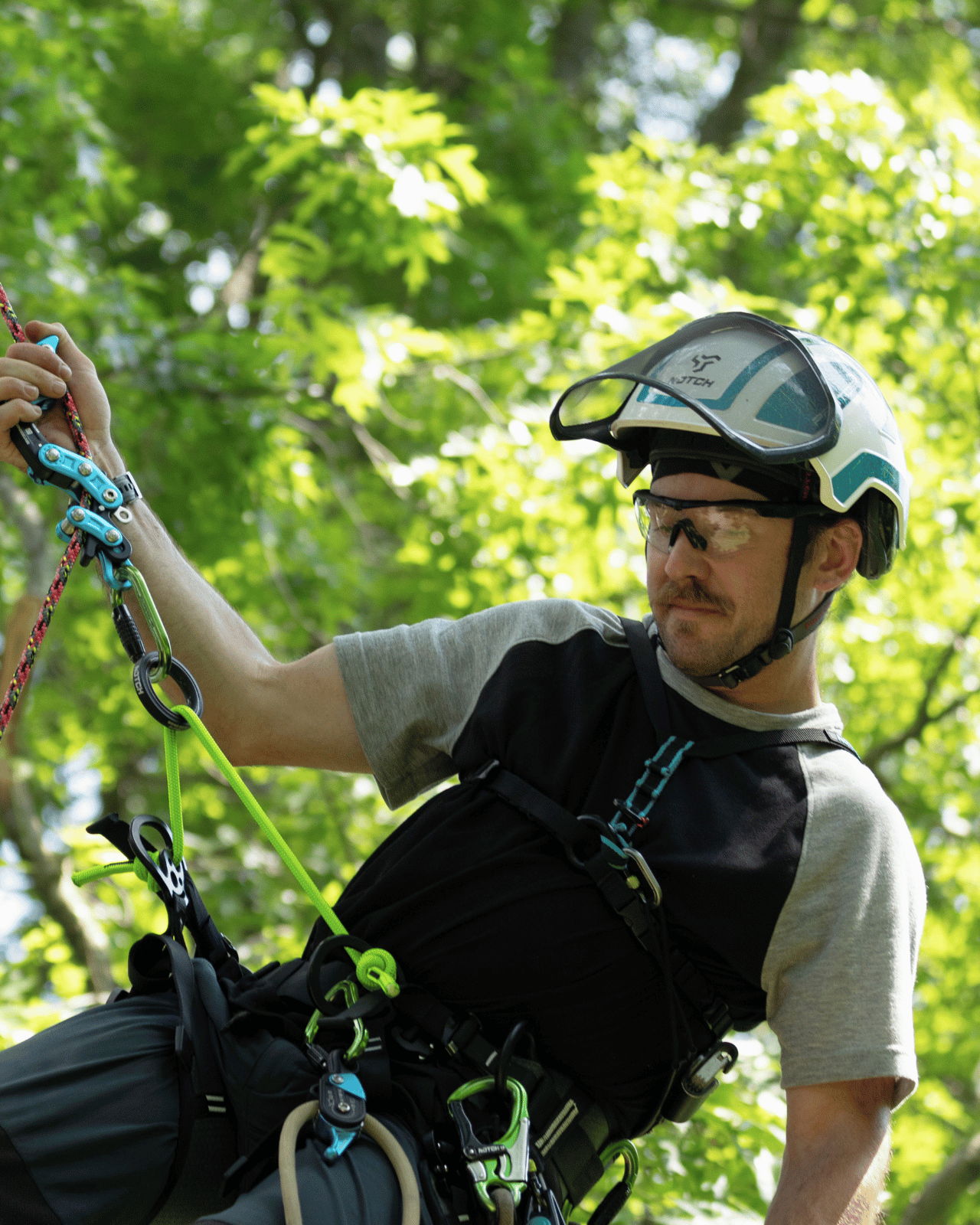 Man climbing with safety gear in a green, leafy environment.