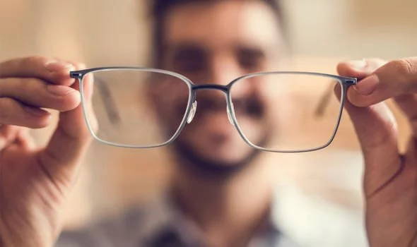 Man putting on prescription eyeglasses with blurred background 