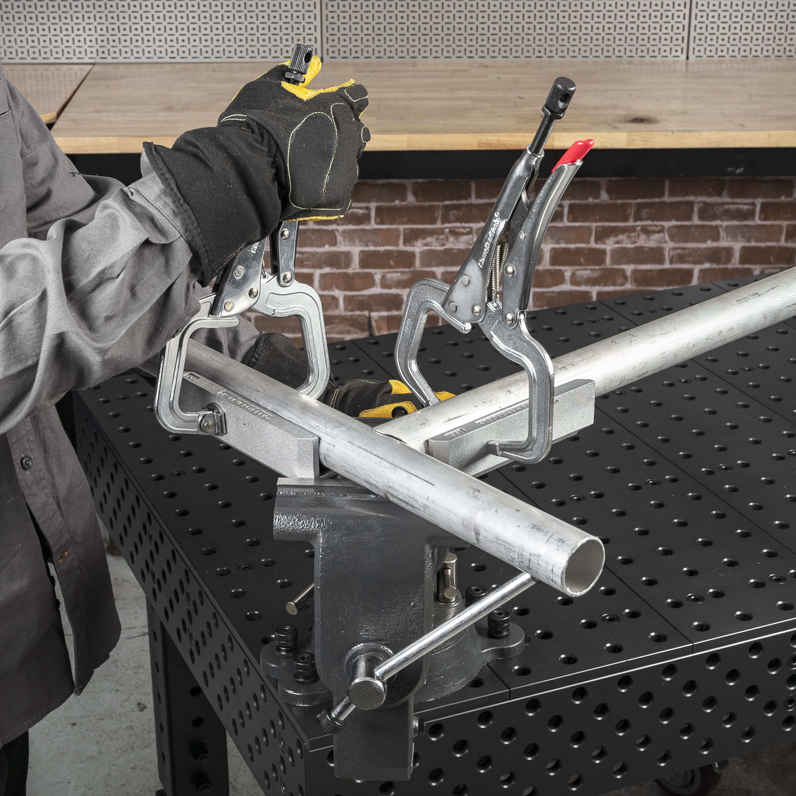 Person using clamps on a metal pipe at a workbench.