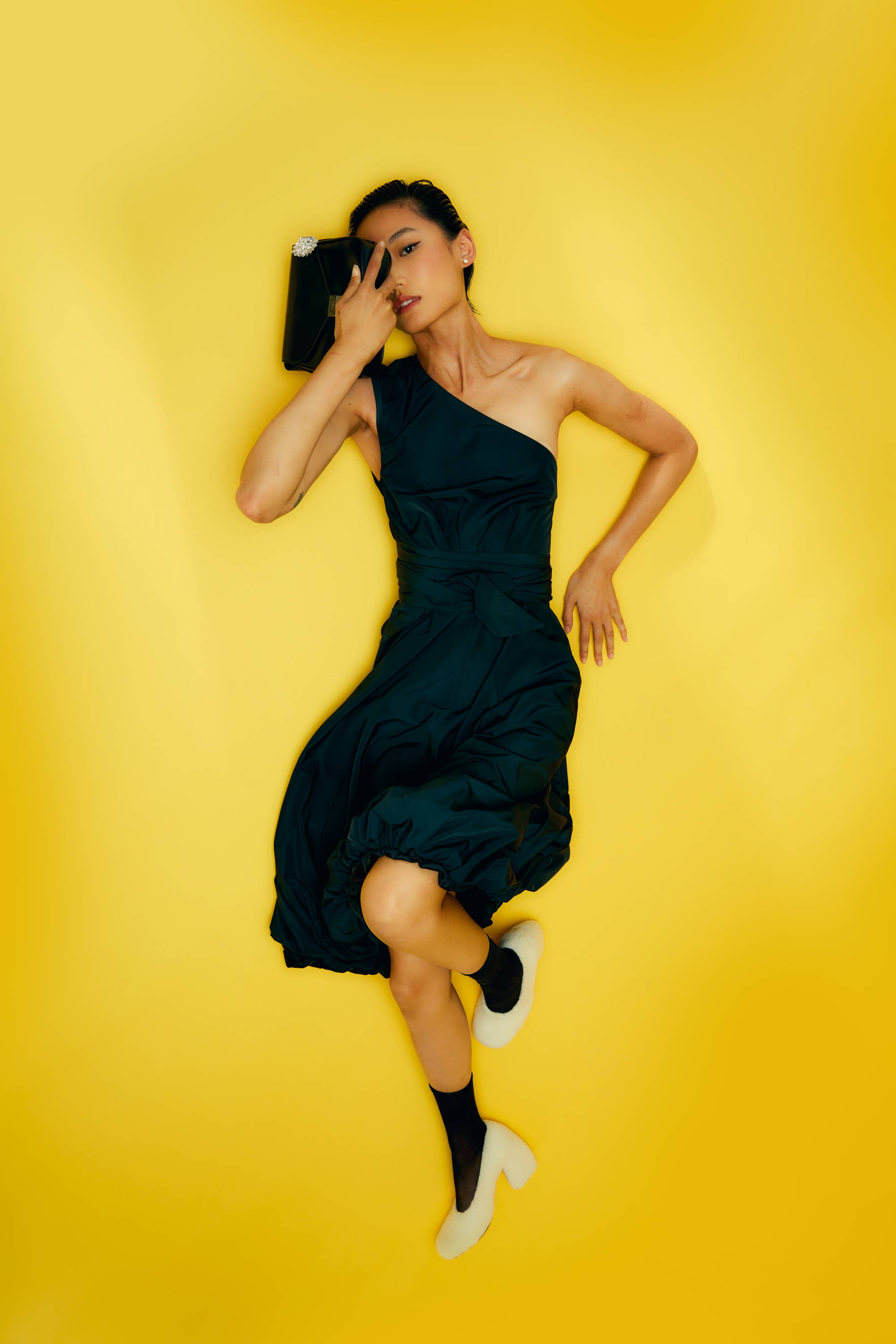 Person in a dark dress lying on yellow background, holding a book.