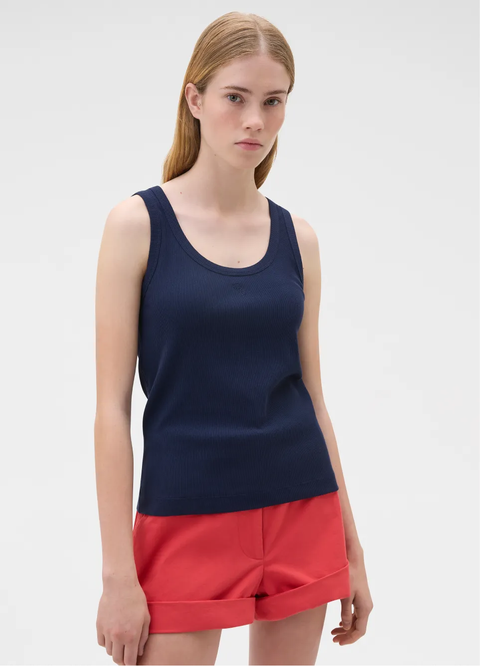 A young woman wearing a navy tank top and red shorts.