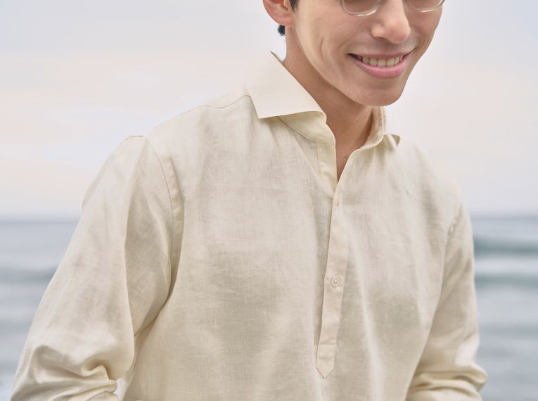 Young man in a light shirt smiling by the ocean.