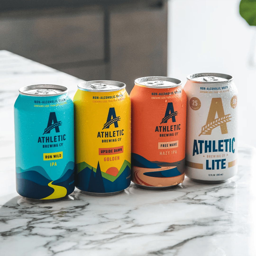 Four cans of Athletic Brewing Company beverages on a marble surface.