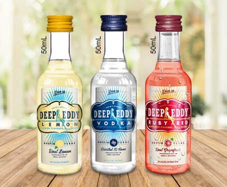 Three bottles of Deep Eddy vodka in various flavors on a wooden table.