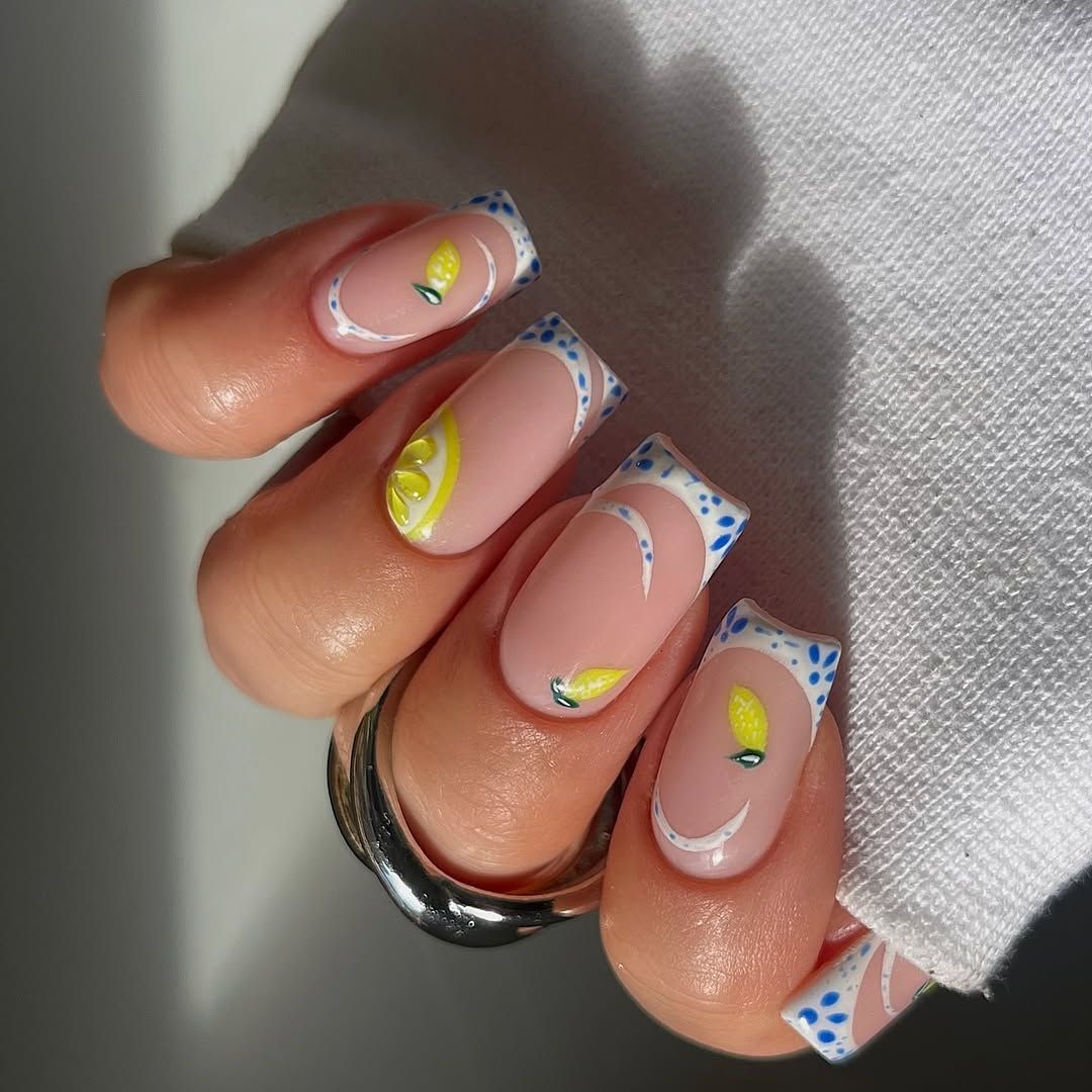A close-up of white French tip nails with blue and lemon accents.