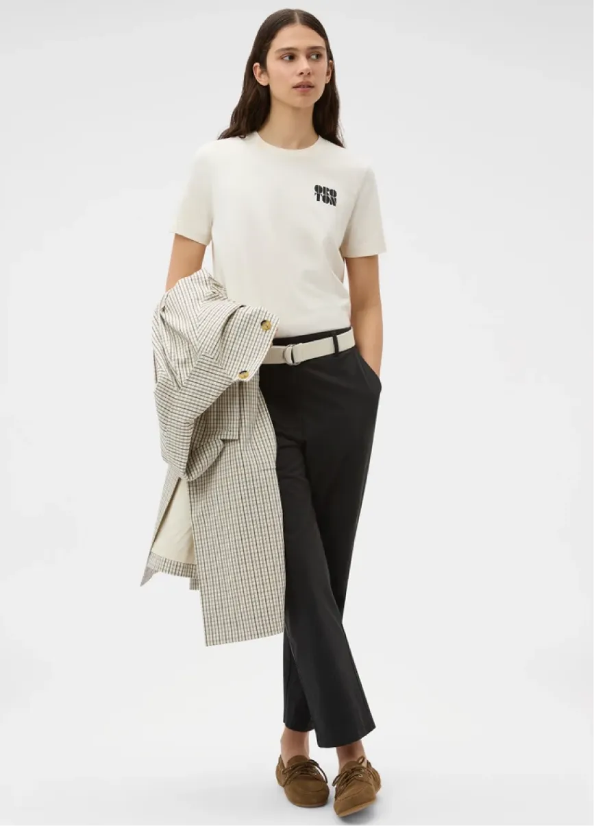 A woman in a white t-shirt and black trousers holding a coat.