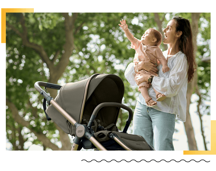 Mother holding baby next to a stroller in a park.