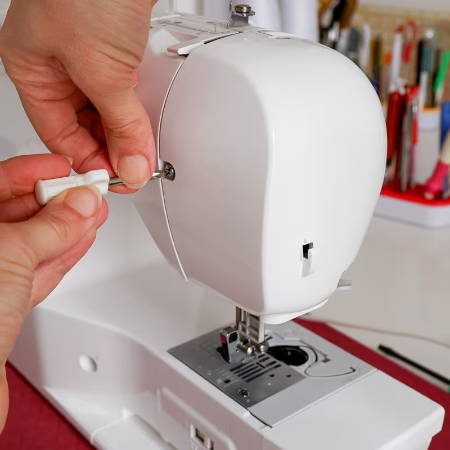 hand with screwdriver to open sewing machine head 