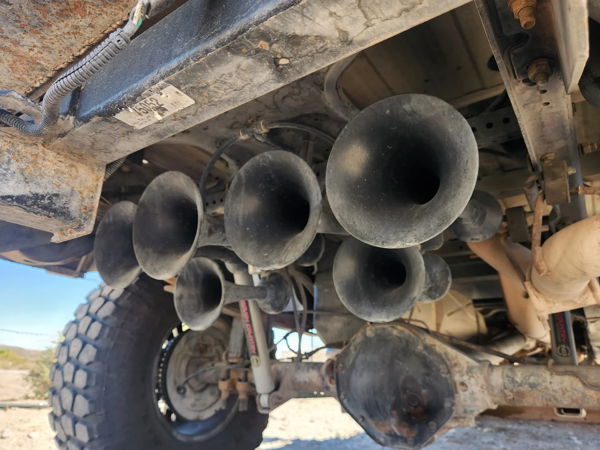 Five-trumpet train horn kit mounted beneath truck bed on lifted Dodge Ram undercarriage