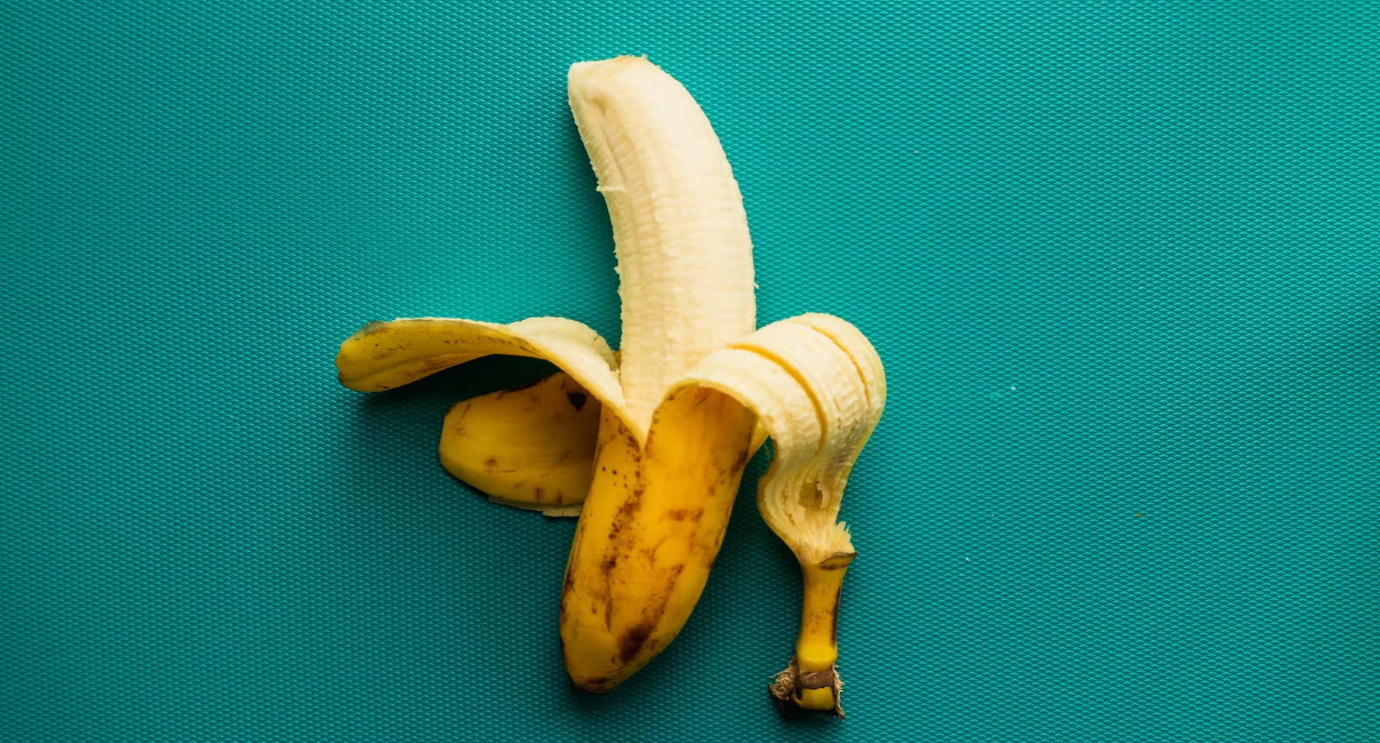 a half-peeled banana against a teal background