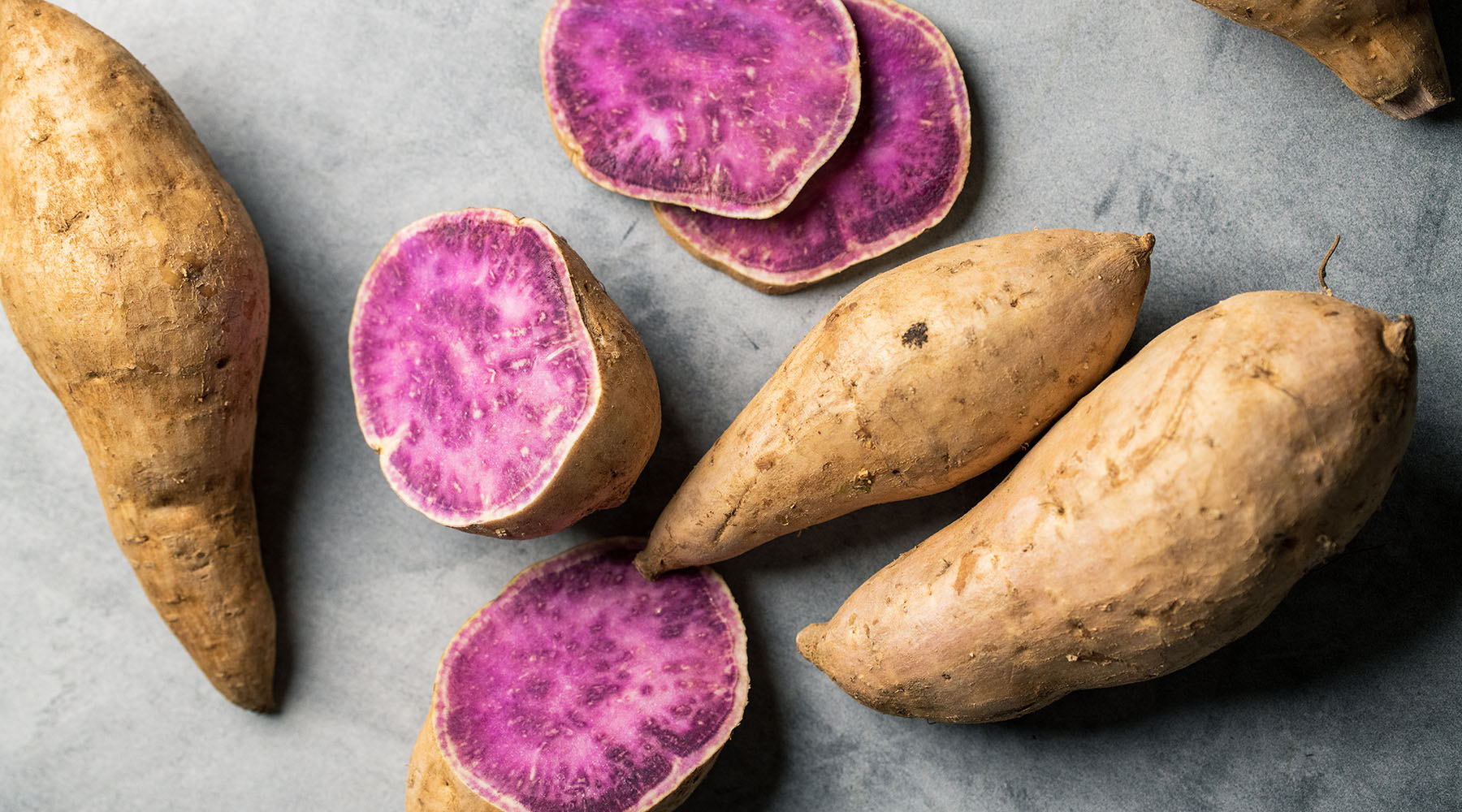 Okinawa Sweet potatoes, some sliced, on a gray surface.