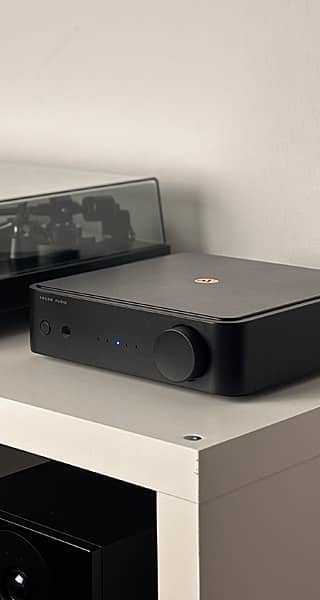 A black audio device on a white shelf next to a turntable.