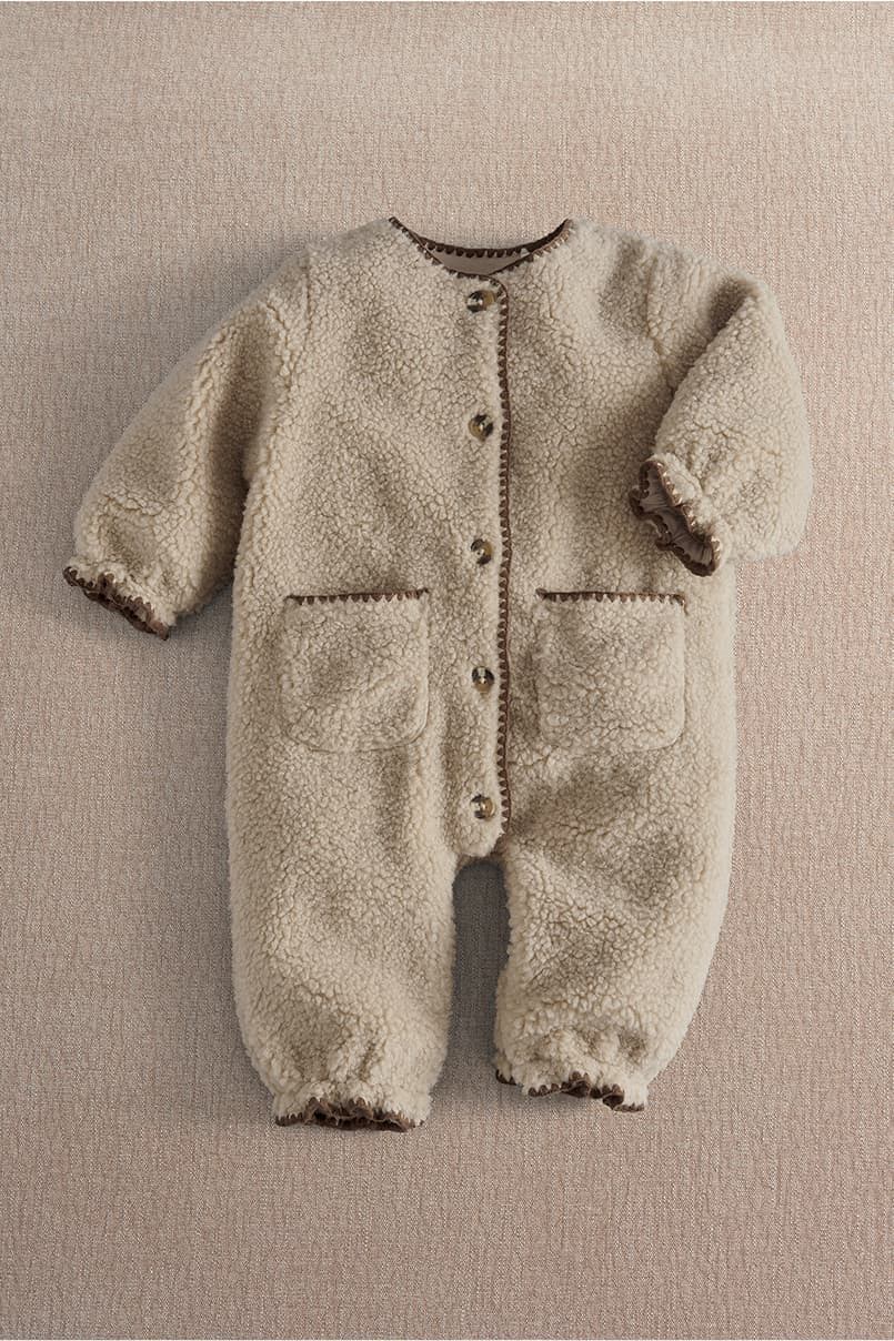 Beige fluffy baby onesie with buttons and pockets on a soft background.