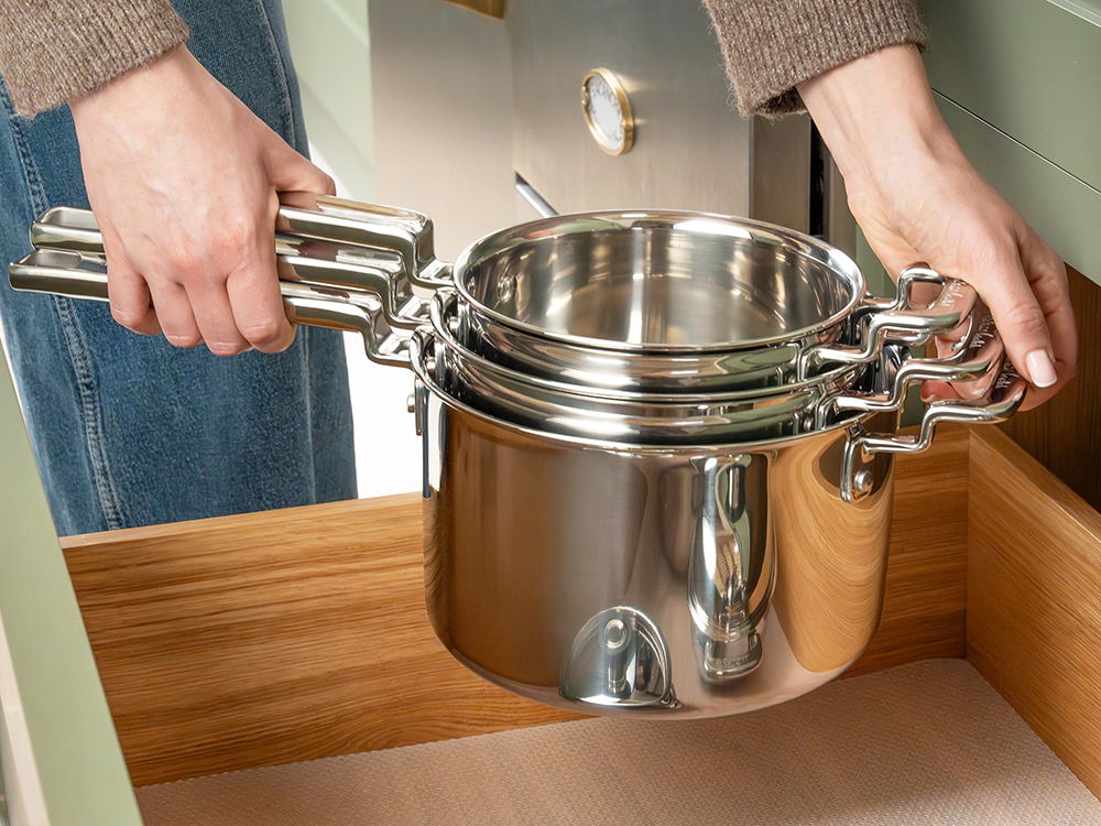 Person holding a stack of 316 Series stainless-steel saucepans above a drawer.