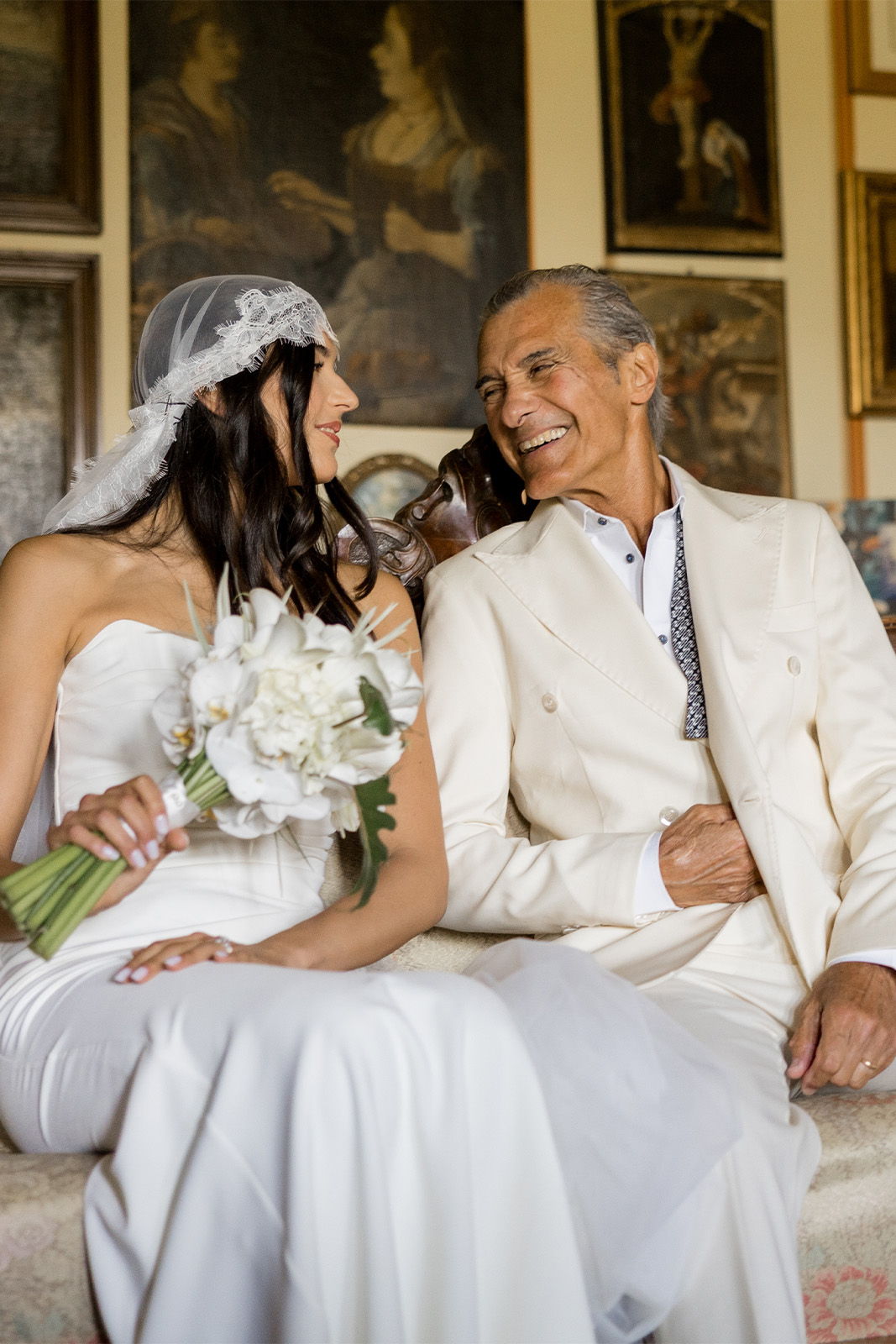 Bride and groom smiling at each other, surrounded by artwork in a cozy setting.