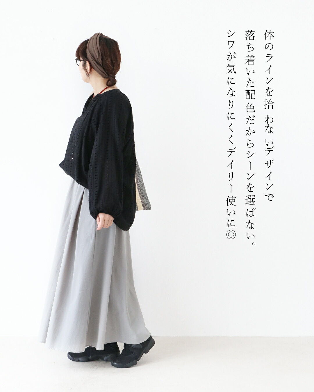 Woman in a black top and gray skirt, standing sideways against a white background.