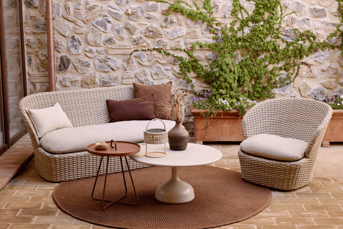 An outdoor lounge area featuring the Coast Loveseat, Coast Swivel Chair, On-The-Move Side Table, Glaze Coffee Table, and Knit Round Outdoor Rug all from Boxhill.
