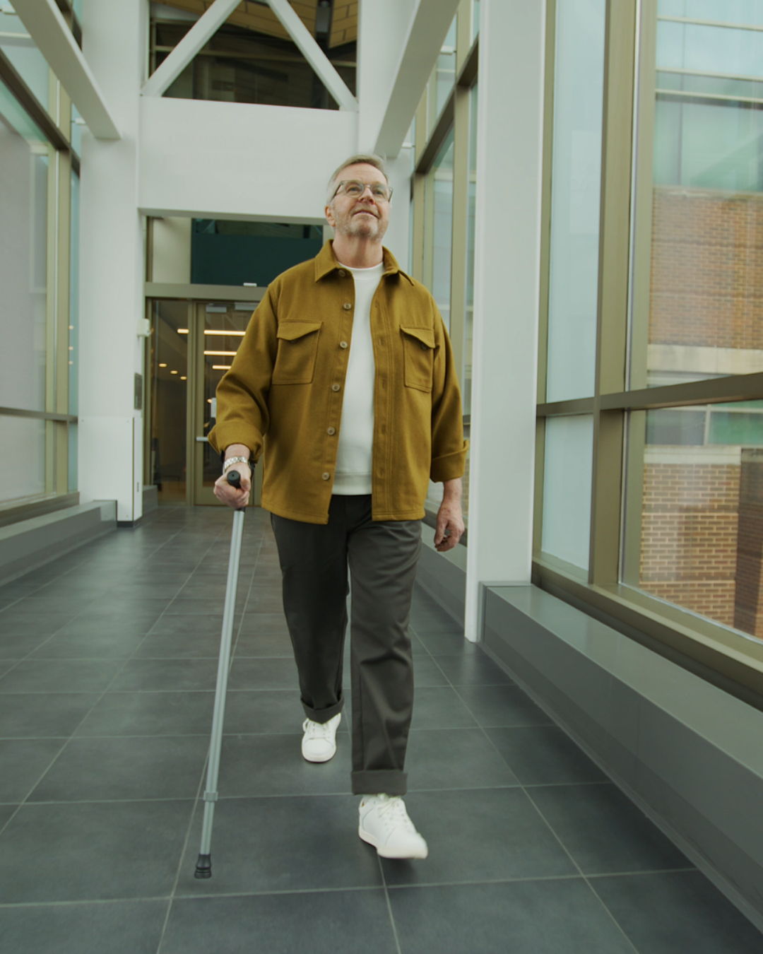Man walking confidently through a hallway using a single Y-Cane in silver finish