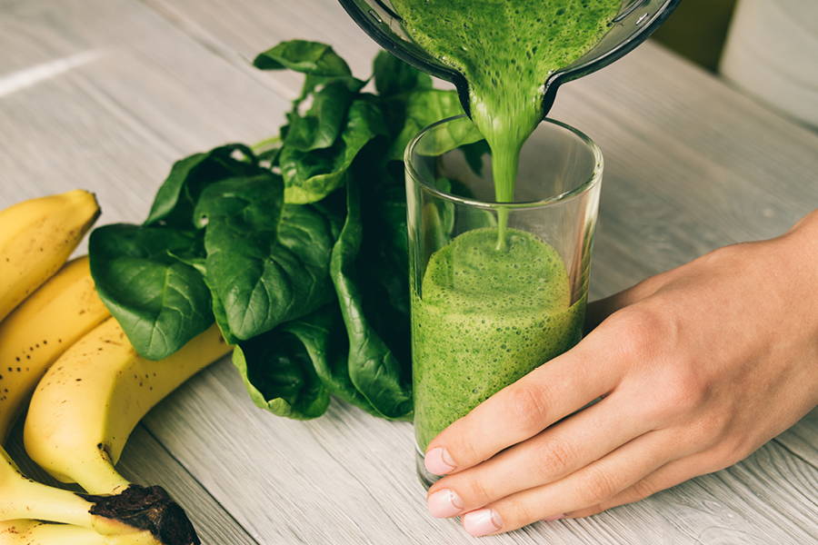 green smoothie being poured into a glass with bananas and spinach leaves beside it