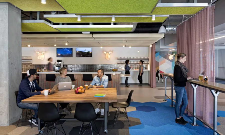 Modern office space with a kitchen area and people working at tables.