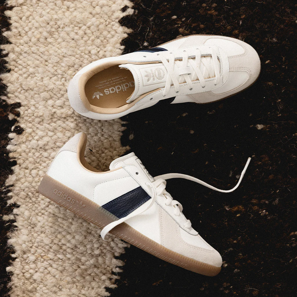 A pair of white sneakers with a navy stripe on a rug.