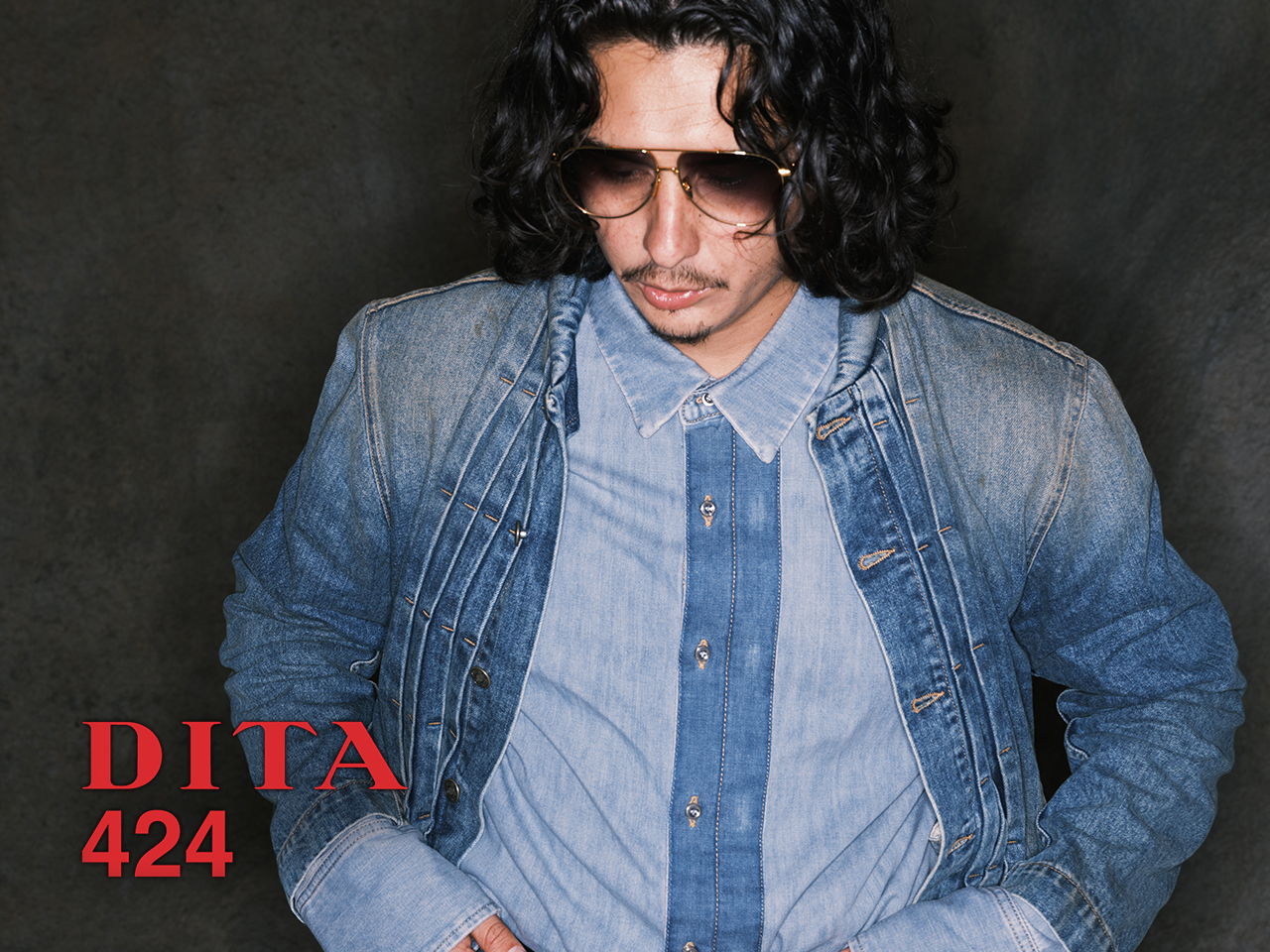 Person with long hair wearing sunglasses against a dark background.
